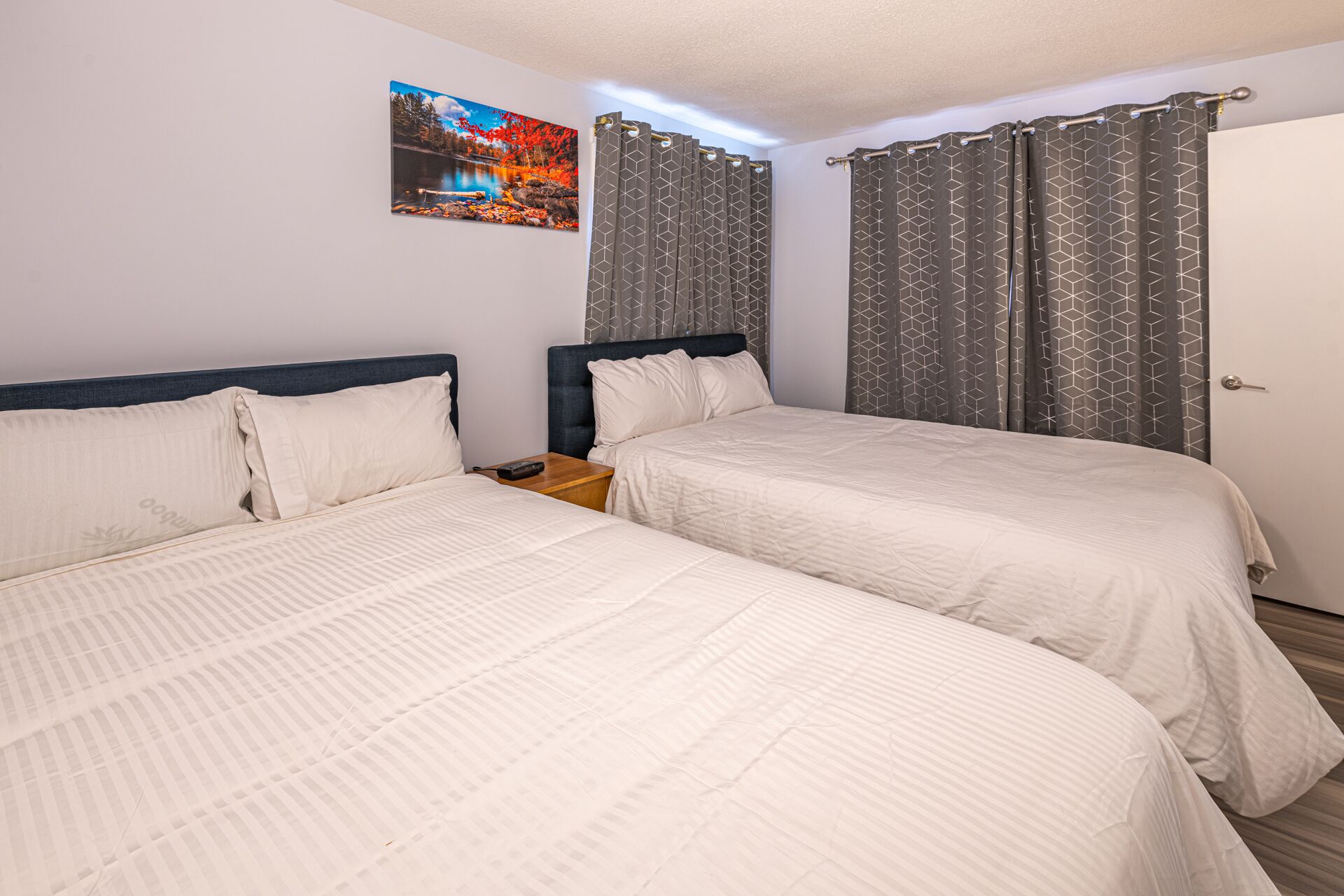 A double room with two beds, a nightstand, a painting on the wall, and patterned curtains.