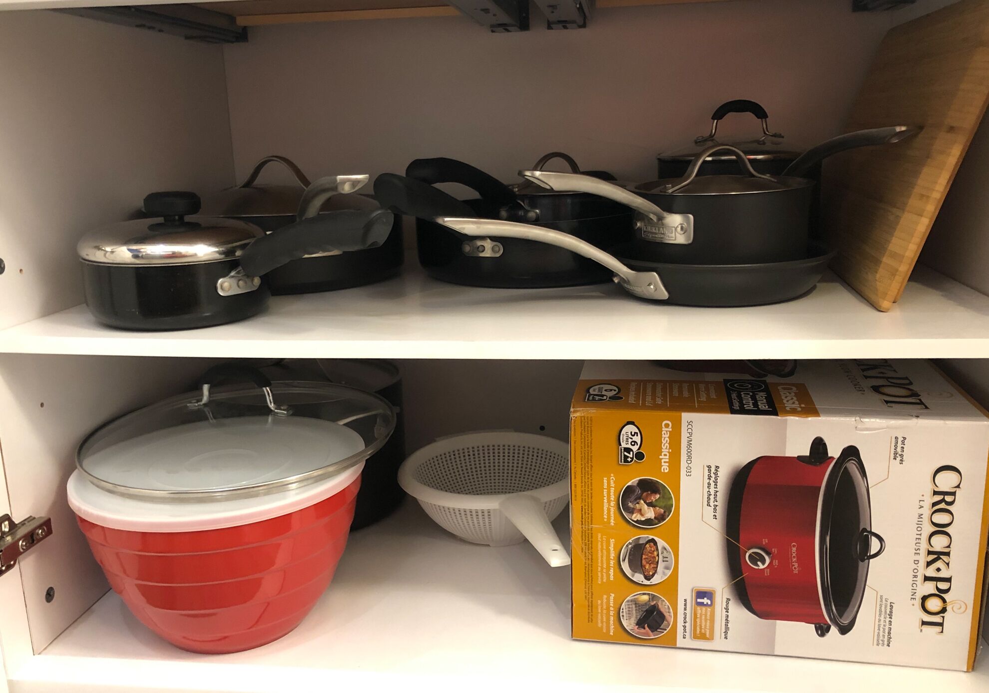 A kitchen shelf with various cookware items including pots, pans, and a colander.