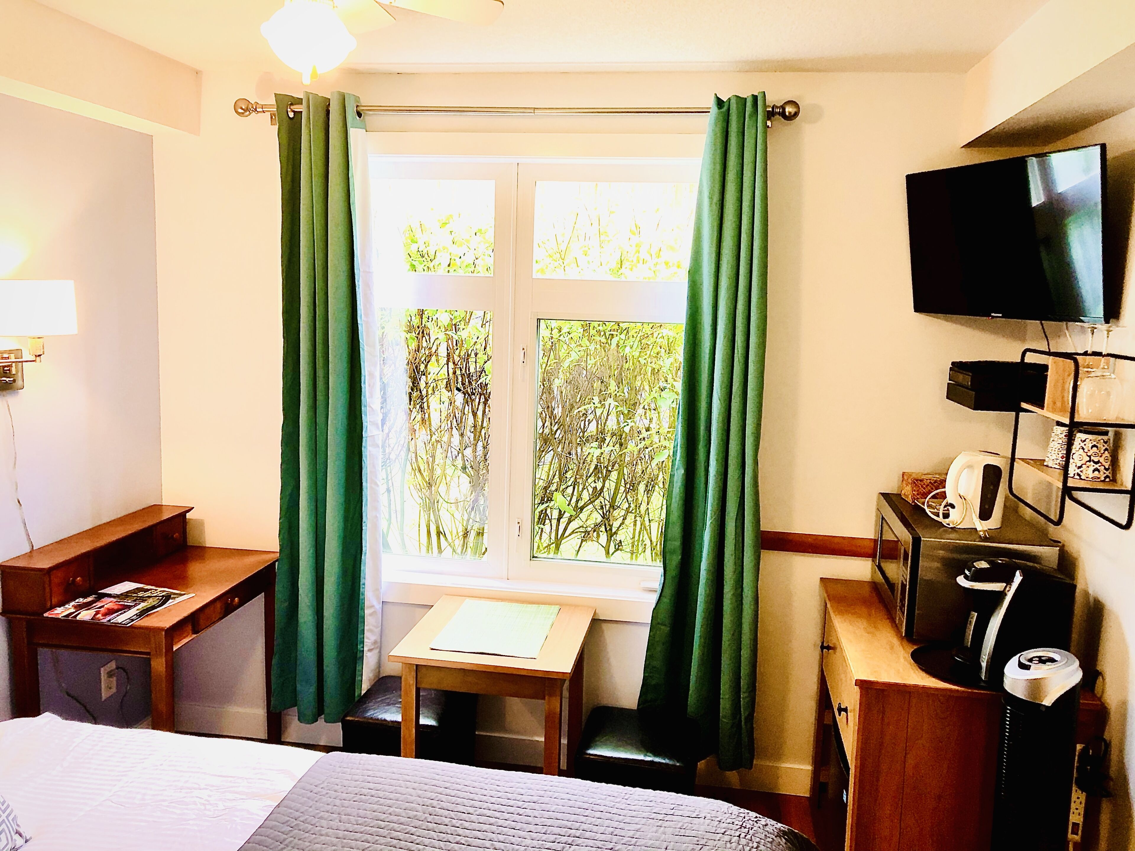 A hotel room with a bed, a desk, a chair, a TV, and a window with curtains.