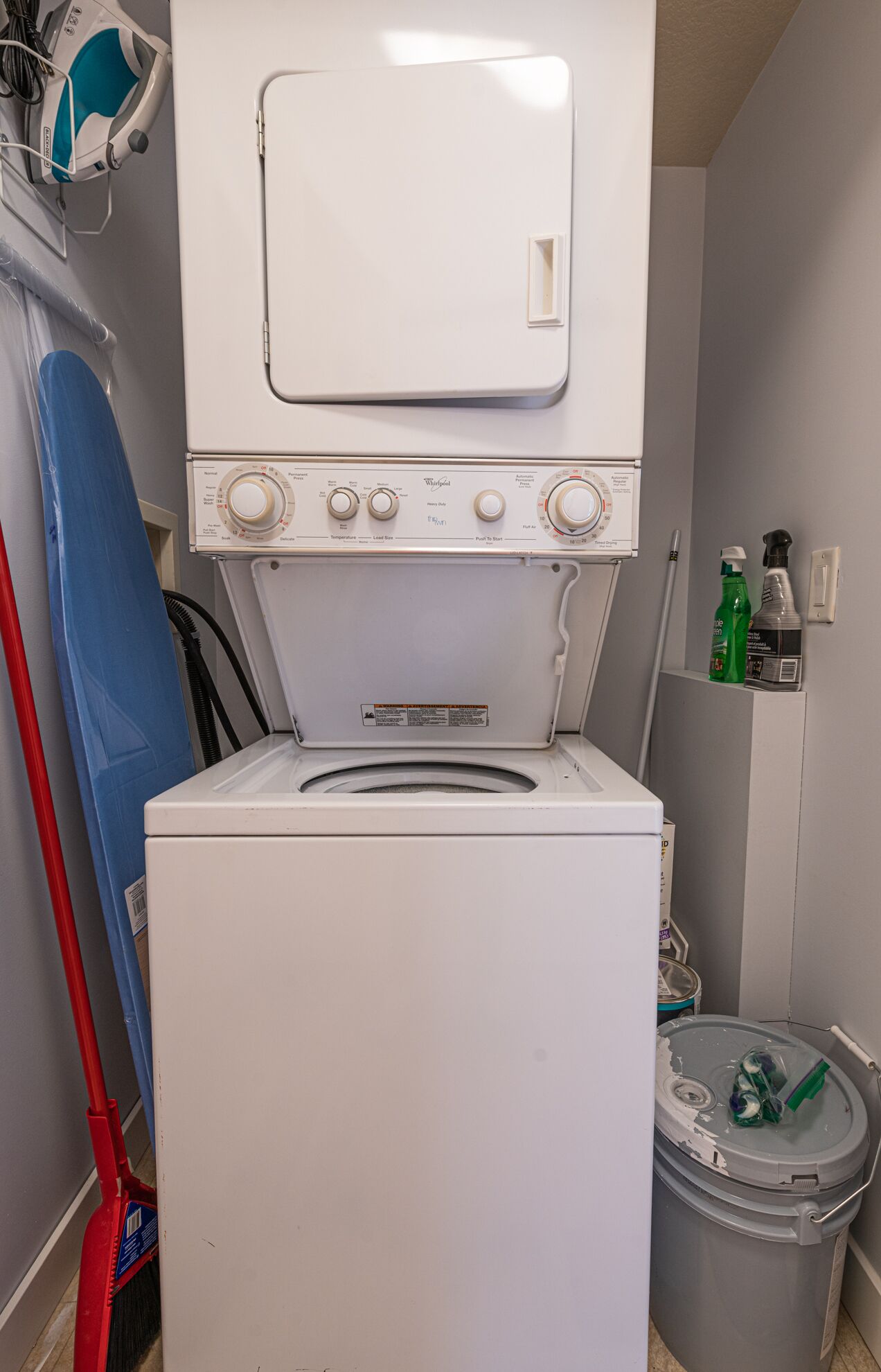 A compact laundry room with a front-loading washer and dryer, a mop, and cleaning supplies.