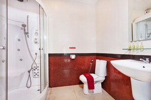 A bathroom with a glass-enclosed shower, a toilet with a red towel, and a sink with toiletries.