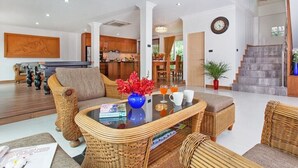 Un salón amplio con muebles de mimbre, una mesa de centro y vistas a la cocina y la escalera.