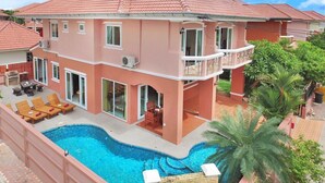Una casa de dos pisos con piscina, mobiliario exterior y un balcón.