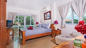 Un dormitorio con cama, mesitas de noche, televisor, ventana con cortinas y vistas al exterior con vegetación.