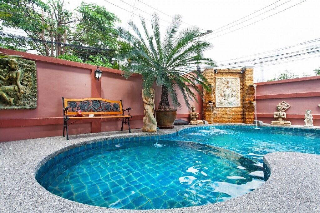 A swimming pool with a stone wall, a bench, and decorative statues.