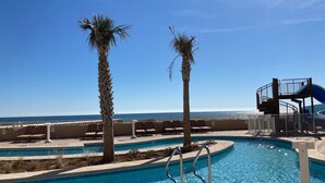 A pool area with a clear view of the ocean, palm trees, and a water slide structure. -  Check out specials for August/Fall stays  ! Spectacular views in newer complex! (Orange Beach)