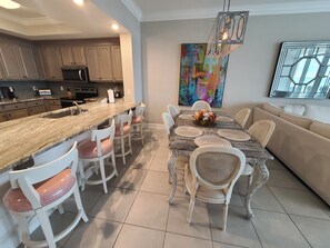 Una cocina moderna con encimera de granito, electrodomésticos de acero inoxidable y comedor con mesa de madera y sillas tapizadas en blanco.