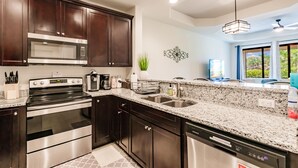 A modern kitchen with dark wood cabinets, stainless steel appliances, granite countertops, and a built-in dishwasher.