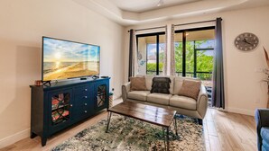 A living room with a television, a sofa, a coffee table, and a large window with curtains.