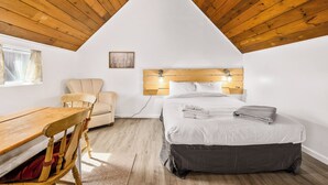Un dormitorio con techo inclinado, una cama con cabecera, una silla, una mesa y una ventana.
