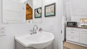 Un baño blanco con lavamanos, espejo y una obra de arte enmarcada.