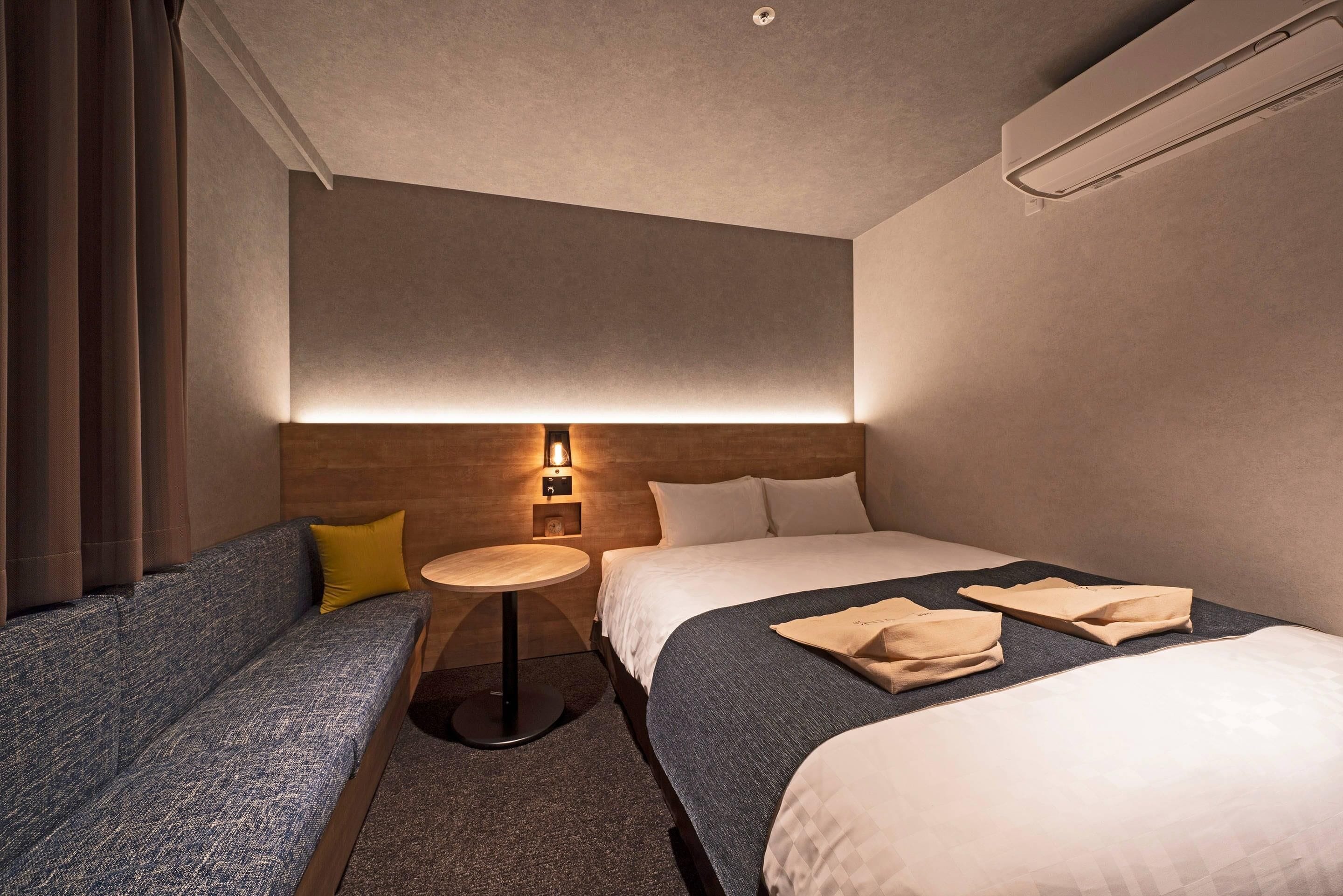 A hotel room with a sofa, a round table, a bed, and a wall-mounted light fixture.