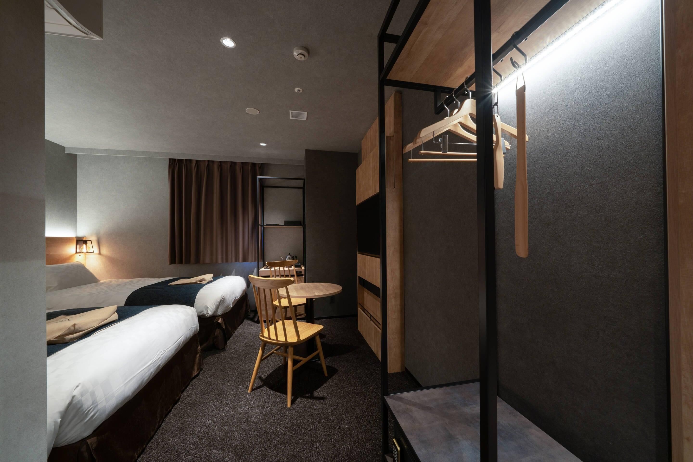 A hotel room with two beds, a small table, a chair, a desk, and a wardrobe.