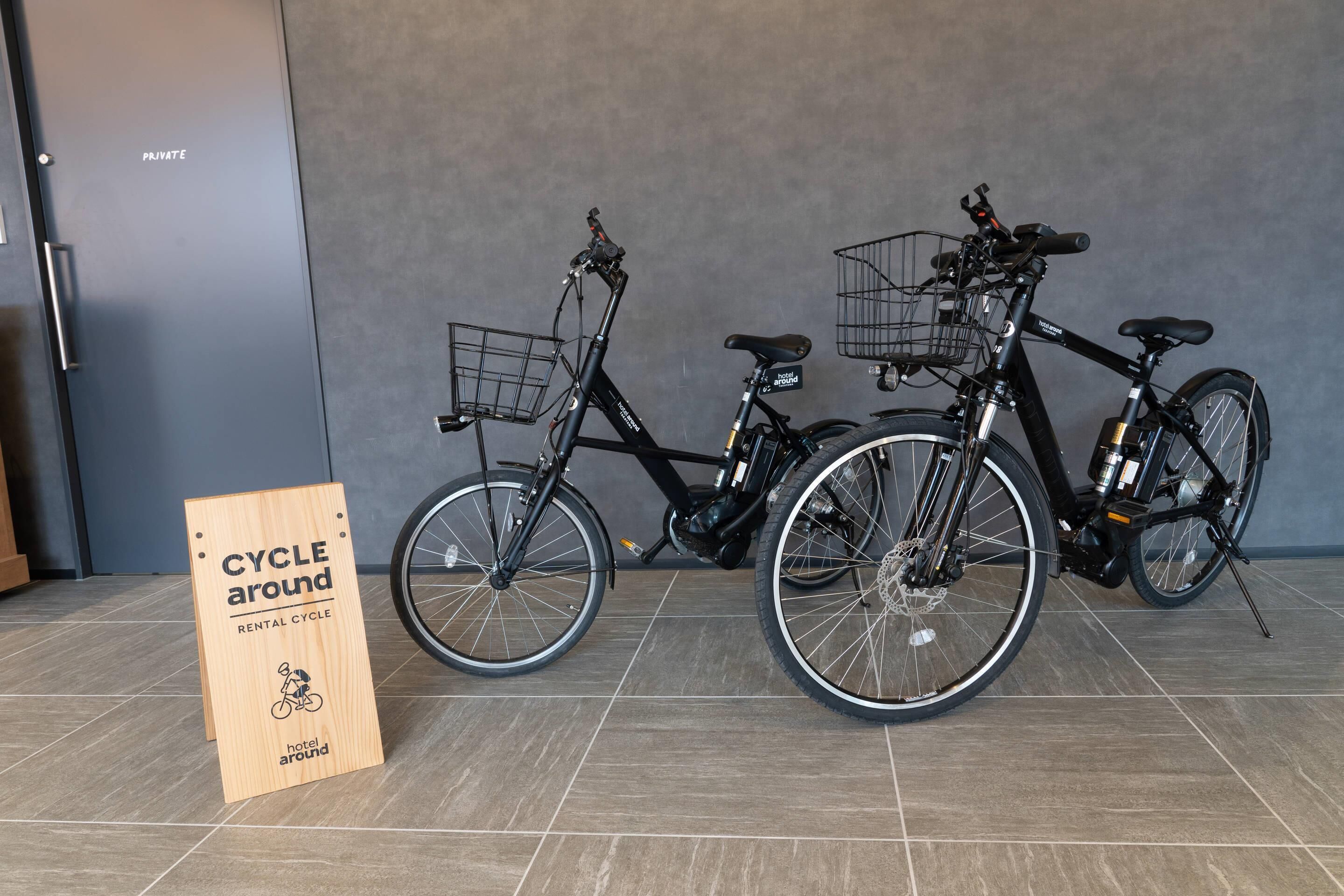 Two bicycles with baskets, a 'CYCLE around' sign, and a 'PRIVATE' door in the background.