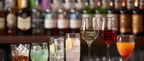 A bar with various glasses of different beverages, including cocktails and water, with a blurred background of bottles.