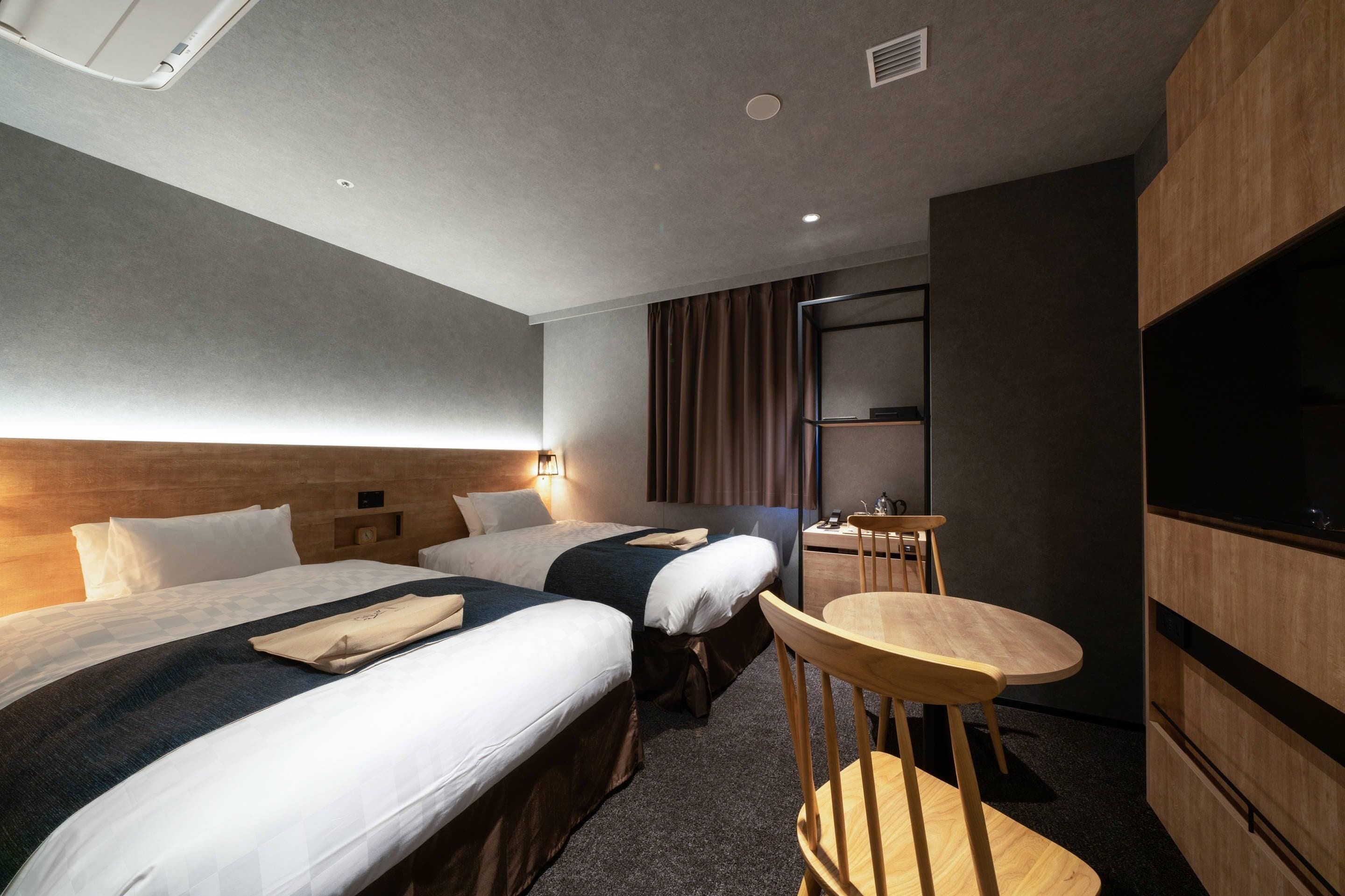 Habitación de hotel con dos camas, una mesita pequeña, una silla, un televisor y un armario de madera.