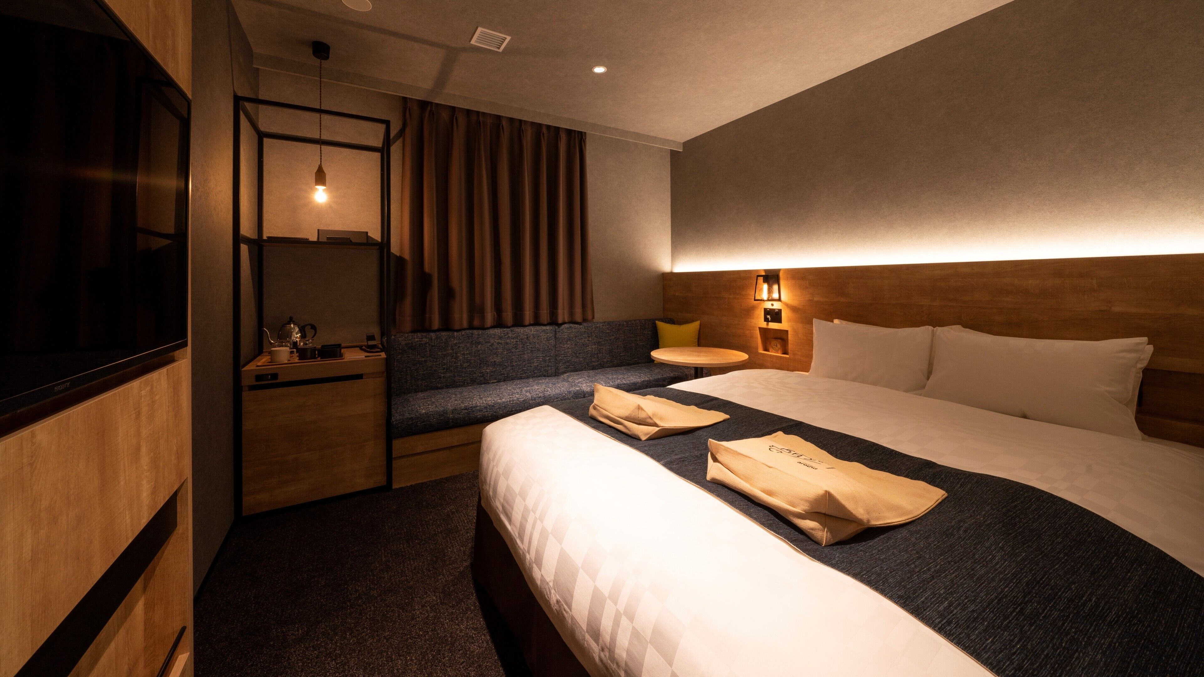Une chambre d’hôtel avec un lit, un canapé, une télévision, une table de chevet et une lampe.