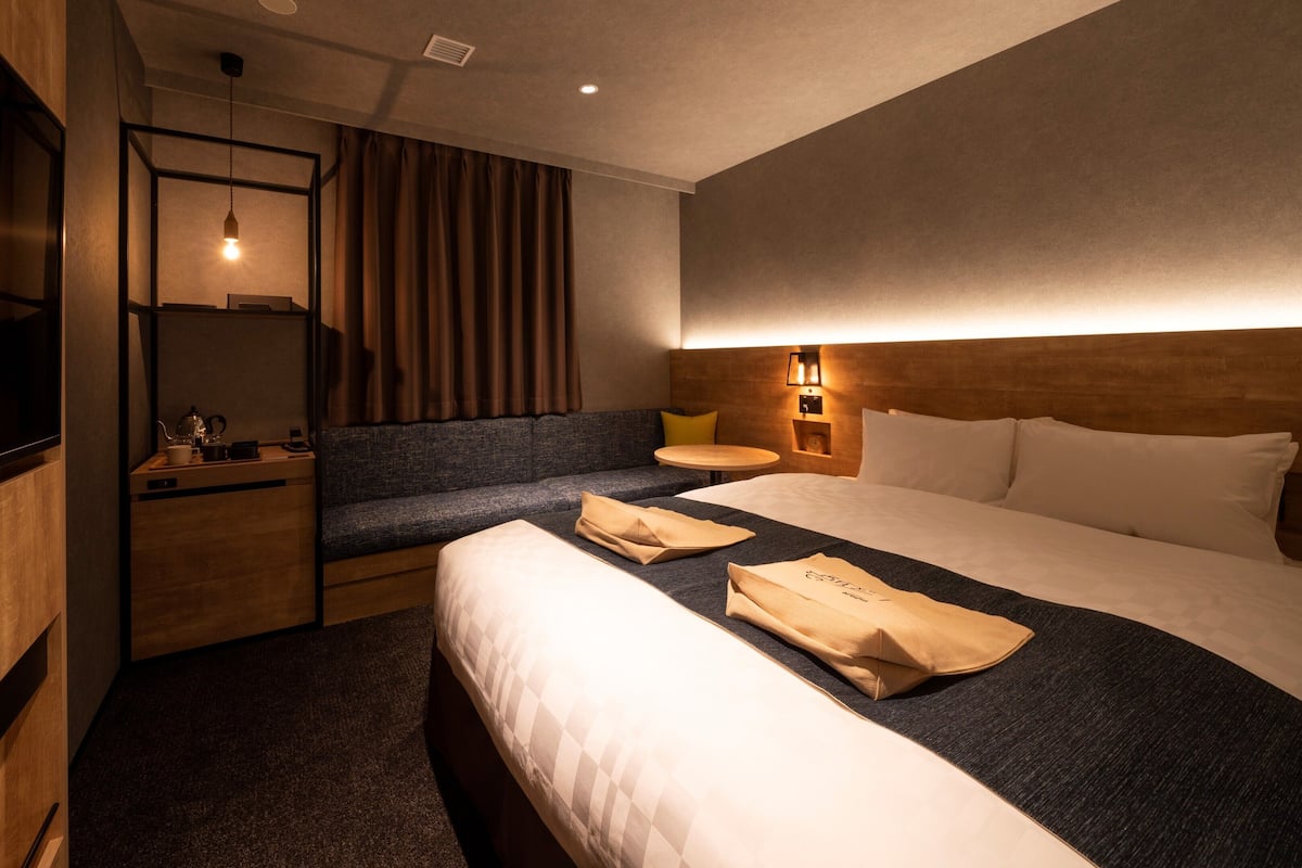 A hotel room with a bed, a sofa, a TV, a bedside table, and a lamp.