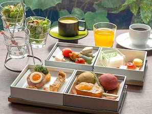 Variedad de alimentos y bebidas dispuestas sobre una mesa, incluyendo ensaladas, sopas y pasteles, con vistas a la vegetación al fondo.
