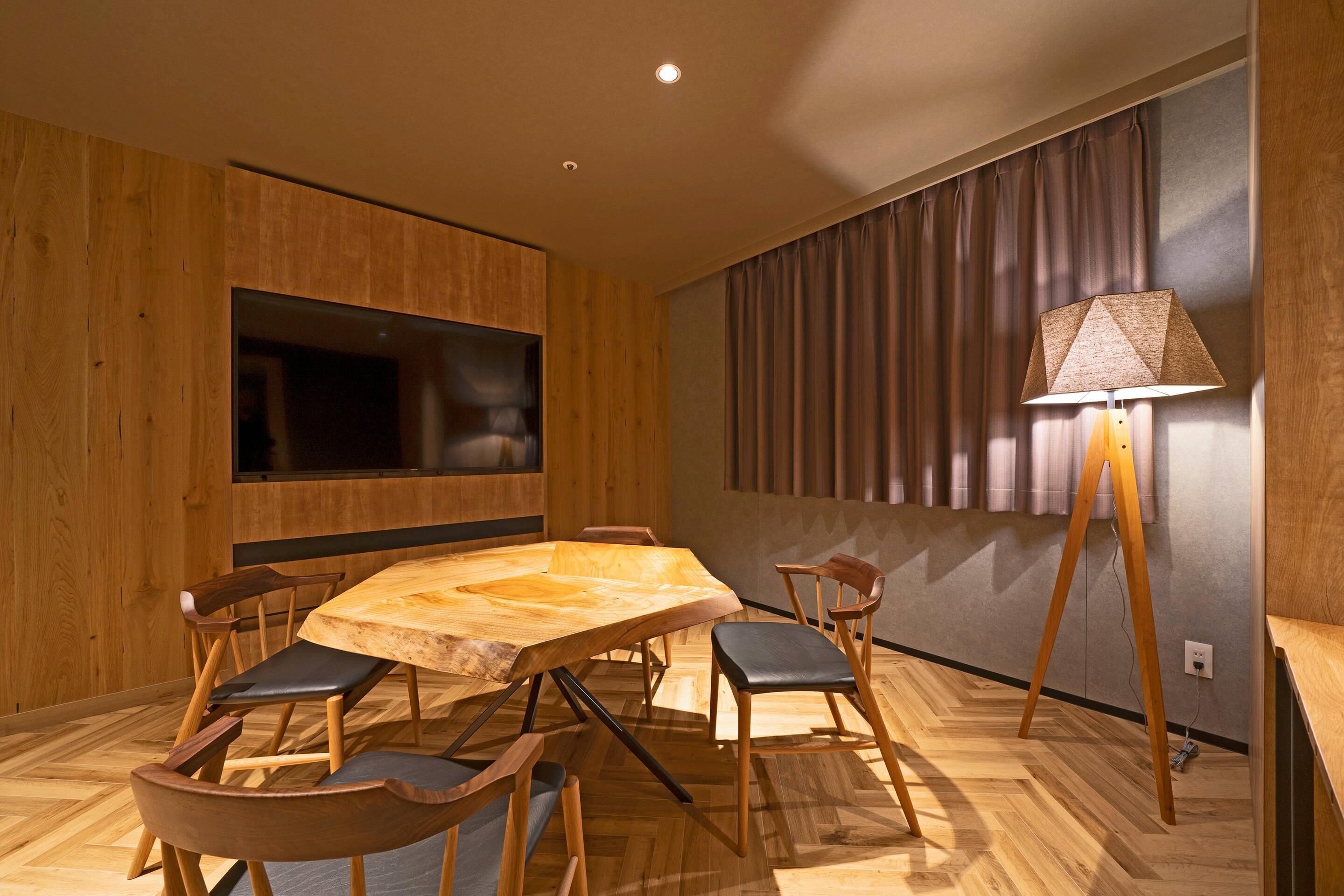 A modern dining area with a wooden table and chairs, a flat-screen TV, and a lamp.