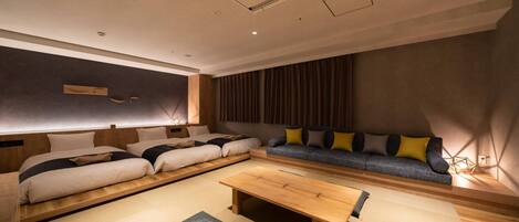A modern hotel room with a large bed, a sofa, a wooden table, and tatami mats.