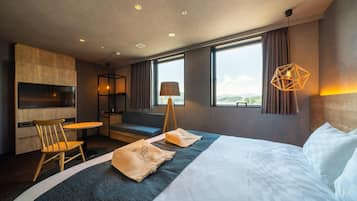 Et moderne hotelværelse med en stor seng, et skrivebord og en stol. Der er to vinduer med gardiner, en lampe og udsigt til det fri.