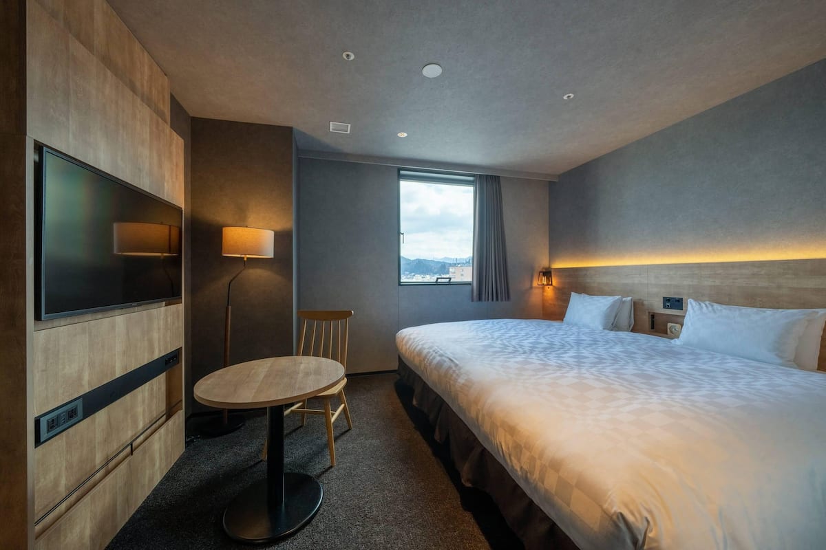 A hotel room with a large bed, a desk with a chair, a TV, and a window with a view.