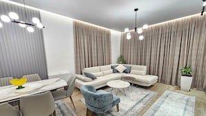 Un salon moderne avec un canapé d’angle, une table à manger avec des chaises, un fauteuil bleu et une plante en pot.