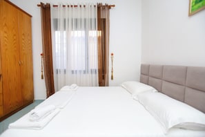 A hotel room with a bed, a wooden wardrobe, and a window with curtains.