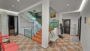 Un vaste espace de vie doté d’un sol carrelé, d’un escalier avec des rampes vertes, d’un coin repas avec des chaises rouges et d’une cuisine équipée d’un réfrigérateur.