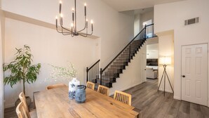 A dining area with a wooden table, chairs, a vase with flowers, a potted plant, and a chandelier. - The Desert Hideaway | Game Room, Pool & Outdoor Kitchen [Free Spa Heating + Early Check-In] (Indio)
