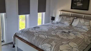 A bedroom with a bed, a nightstand, and a window with a view of greenery. - 4 bedrooms, large deck, park views (Coronet Bay)