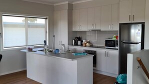 A modern kitchen with a central island, stainless steel appliances, and light-colored cabinetry. - 4 bedrooms, large deck, park views (Coronet Bay)