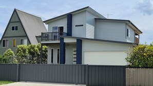 A two-story house with a garage, a fenced yard, and a clear sky. - 4 bedrooms, large deck, park views (Coronet Bay)