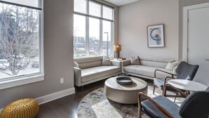 A modern living room with a large window, a sofa set, a coffee table, and a chair. - South Slope Skyhaus with Rooftop Terrace (Asheville)