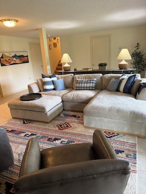 A living room with a sectional sofa, a coffee table, a patterned rug, and a staircase in the background. - Serene mountain escape with beautiful views and a hot tub (Jefferson)