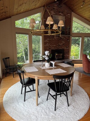 A dining area with a round table, chairs, a chandelier, and a brick fireplace. - Serene mountain escape with beautiful views and a hot tub (Jefferson)