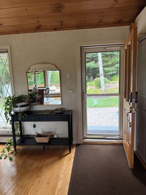 A room with a wooden floor, a console table with a mirror, a door leading outside, and a view of a garden. - Serene mountain escape with beautiful views and a hot tub (Jefferson)