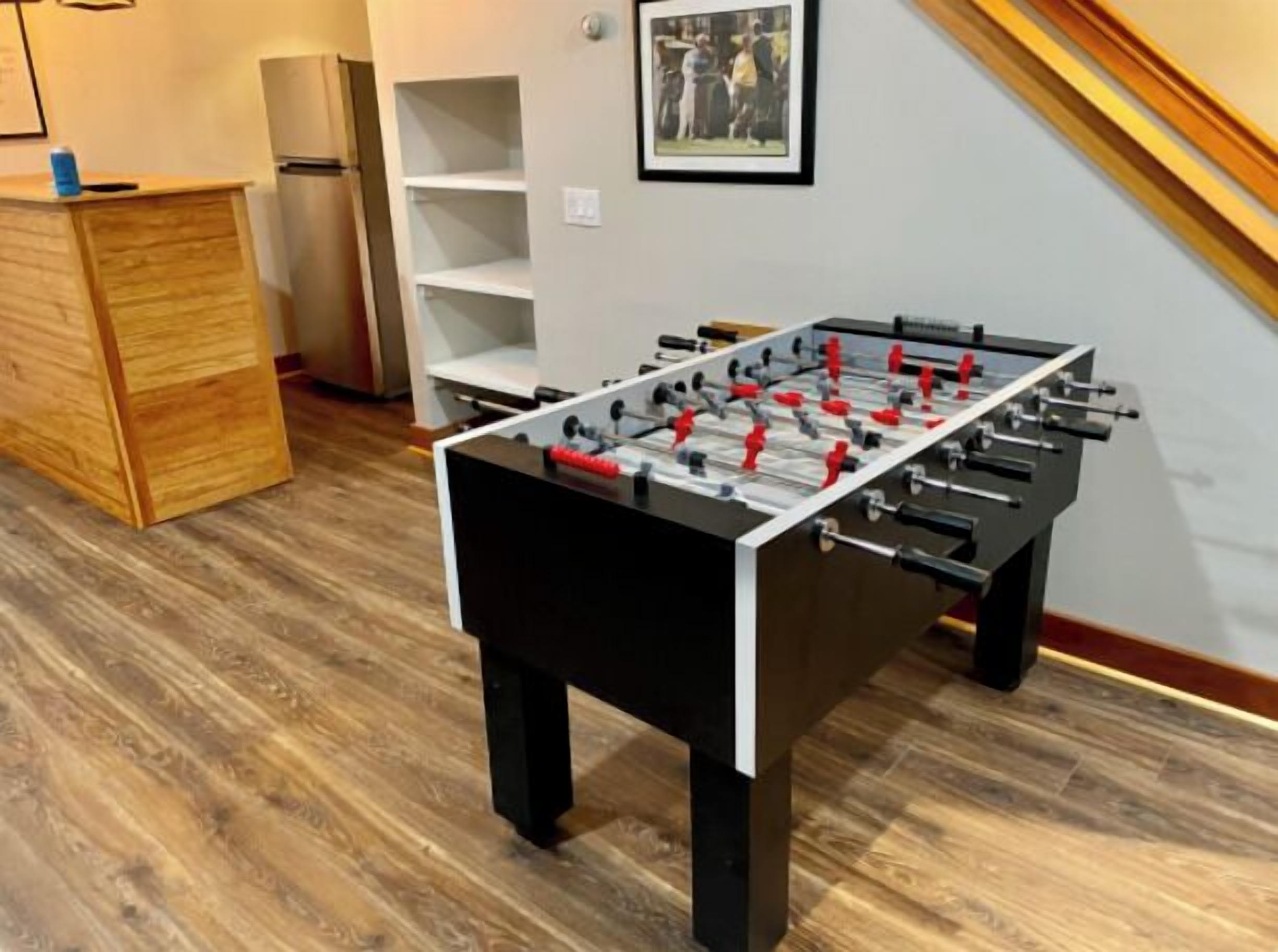 A foosball table in a room with wooden flooring, a wooden cabinet, and a white shelf unit.