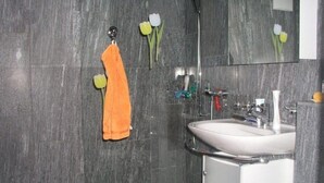 Une salle de bain avec un lavabo blanc, des murs recouverts de carreaux foncés et une serviette suspendue à un crochet.