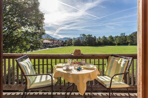 A deck with a table set for two, overlooking a grassy field and distant mountains.