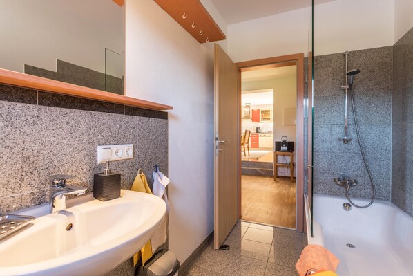 A modern bathroom with a granite countertop sink, a shower, and a visible door leading to another room.