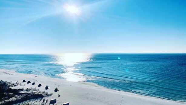 A beach with a clear sky and the sun shining.