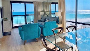 A modern hotel room with a balcony overlooking the ocean, a glass dining table, and a comfortable seating area.