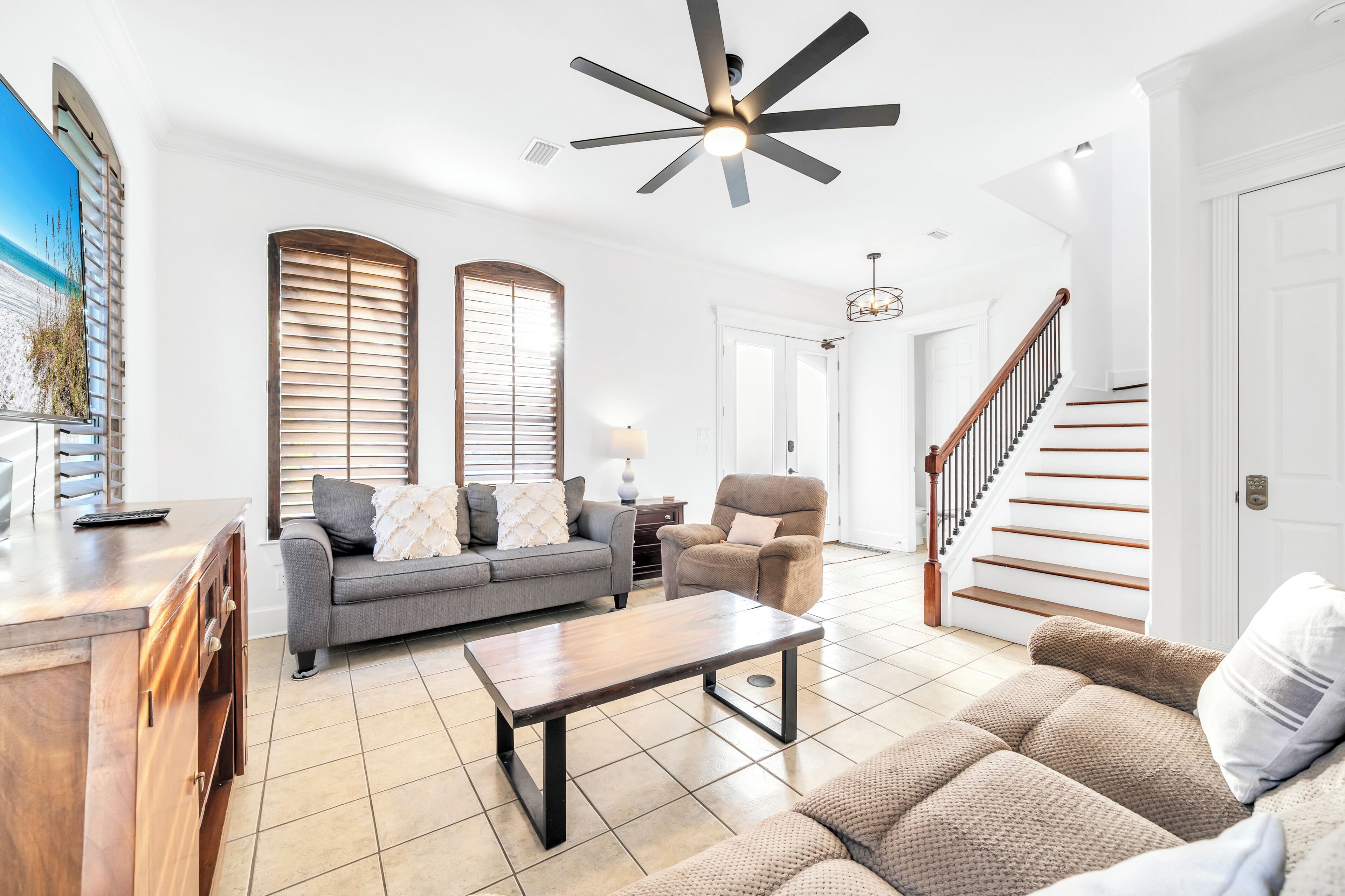A spacious living room with a sofa, armchair, and coffee table, a staircase, and a ceiling fan.