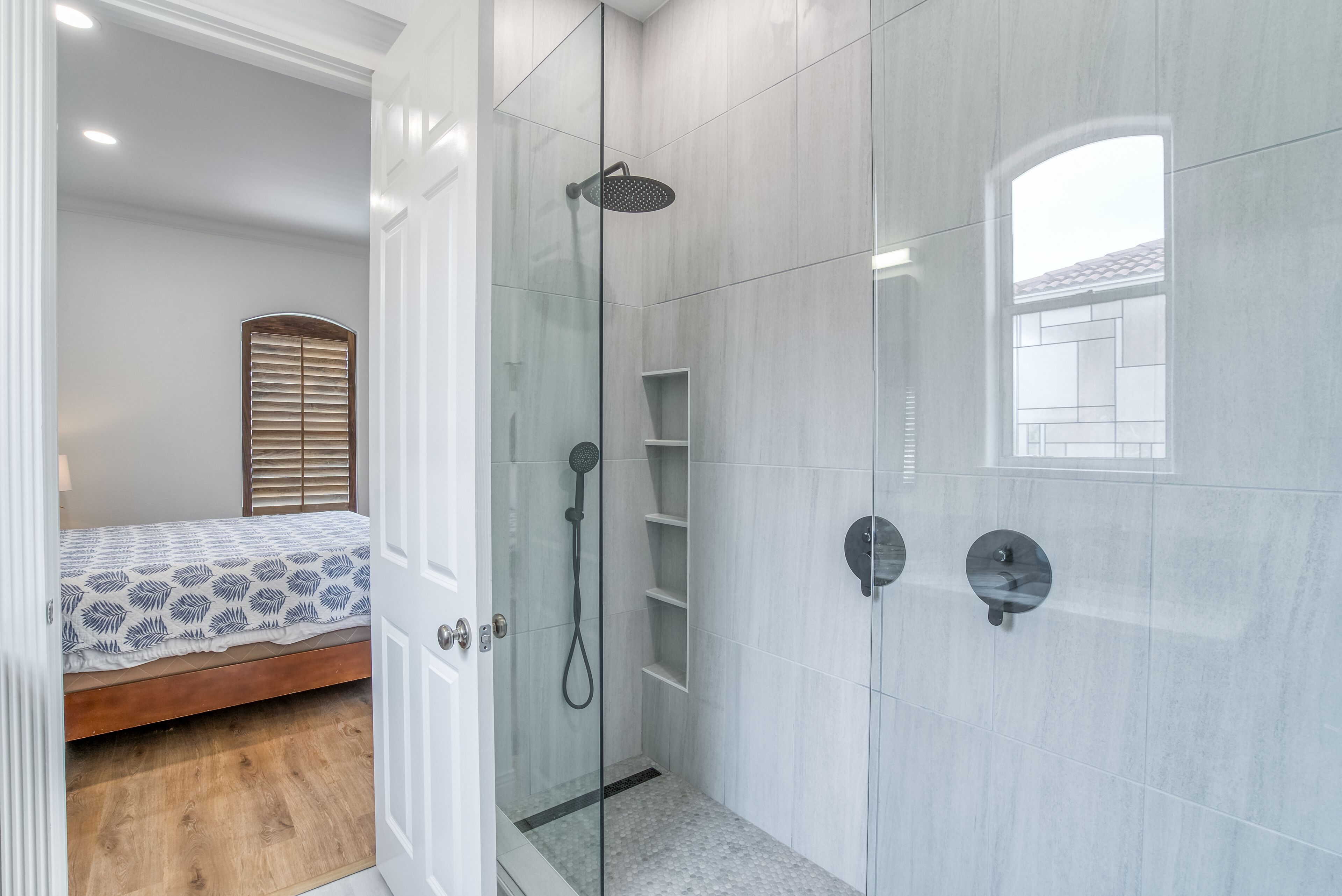 A modern bathroom with a glass shower enclosure, a wooden bed, and a white tiled floor.