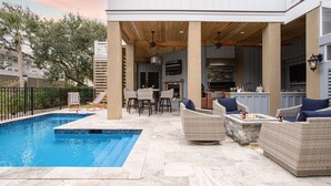 Un área de piscina con jacuzzi, mobiliario exterior y zona de cocina.