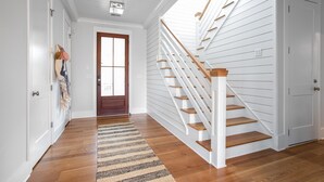 Un pasillo con piso de madera, un tapete a rayas, una escalera blanca con escalones de madera y una puerta con ventanal.