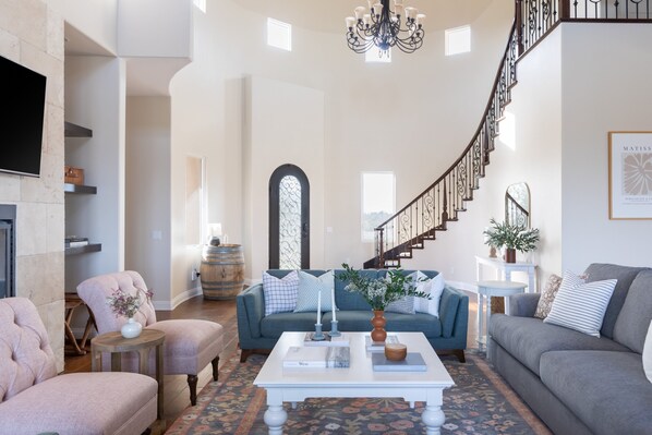 Un salon spacieux doté d’une cheminée, d’un escalier et d’un lustre.