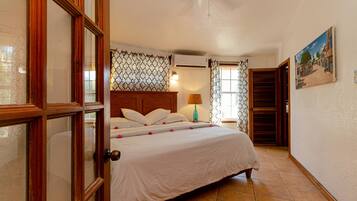 Un dormitorio con cama, ventilador de techo, ventana con cortinas y un cuadro en la pared.